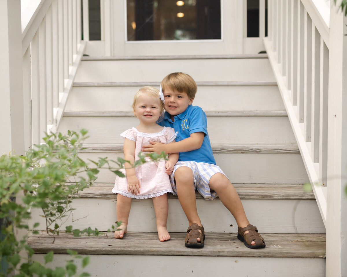 A big brother hugs his toddler sister while sitting on old wooden stairs outside
