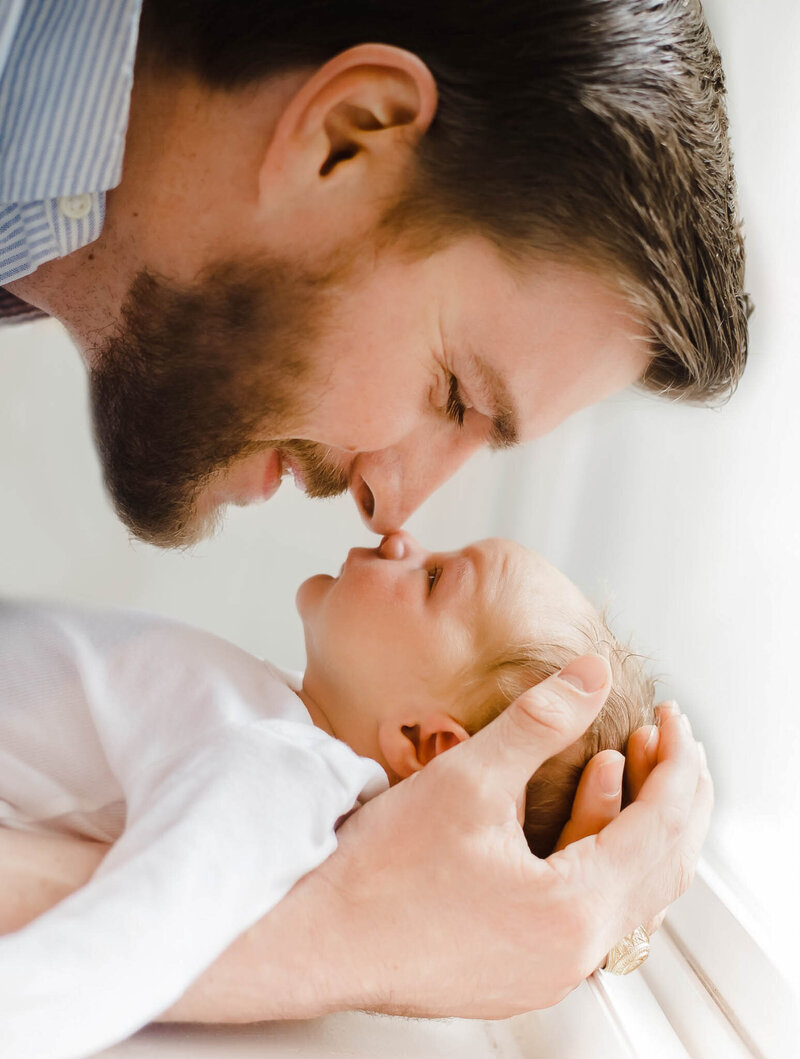 A father presses his nose against his newborn baby's nose while it lays in his arms Greensboro pediatricians